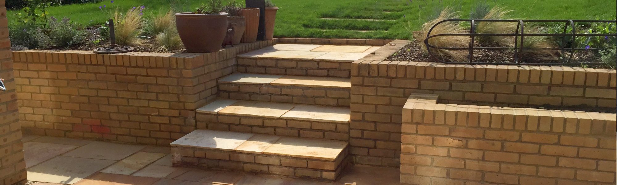 Retaining wall with planters and steps leading from slabbed patio to garden